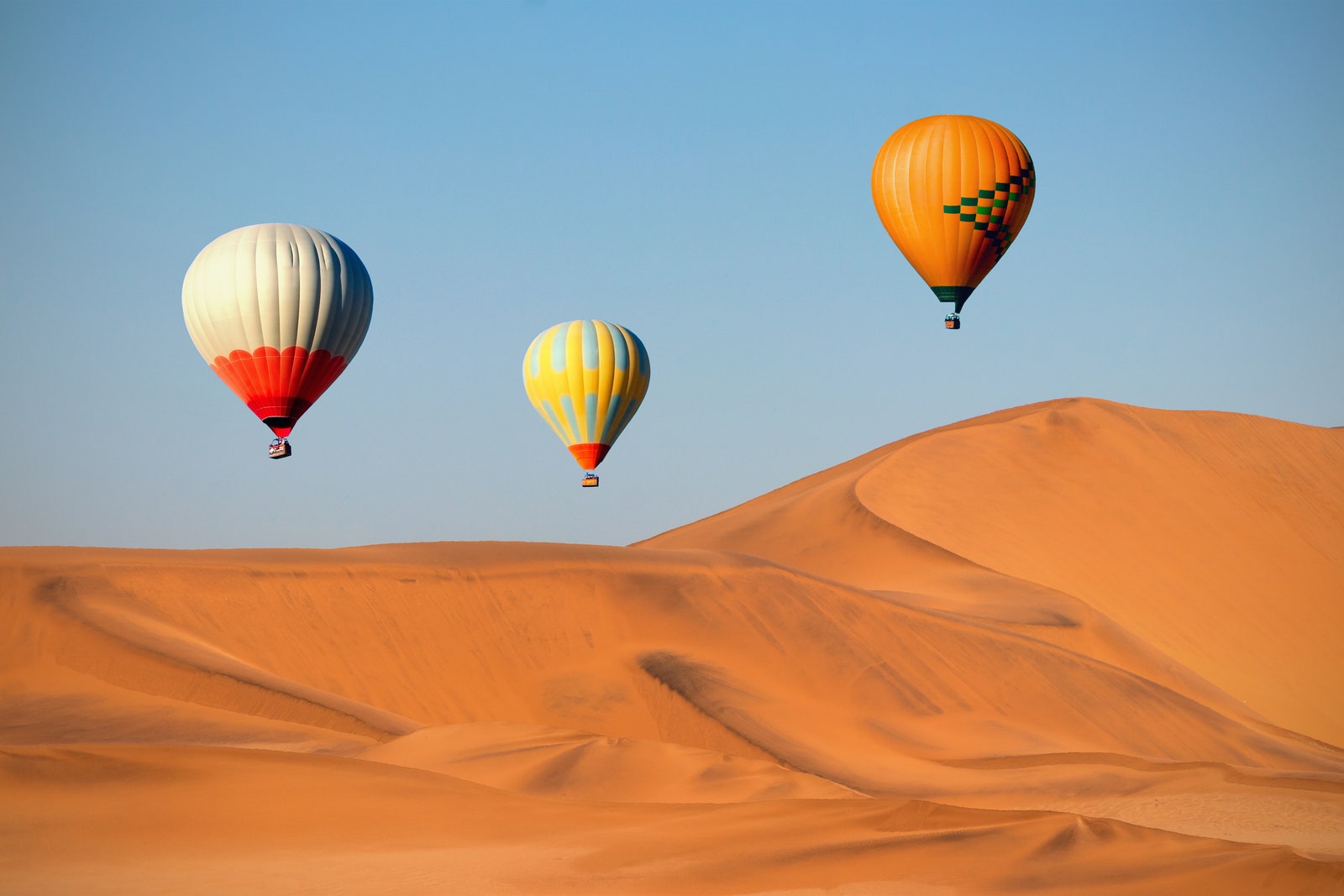 Colored hot air balloons flying over the sand dunes at sunset